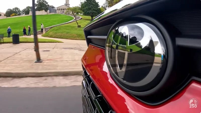 screenshot of a car's grille that takes up half the screen, with a giant Toyota logo dominating the picture and some history place on a grassy hill in the background. screenshot of a car's grille that takes up half the screen, with a giant Toyota logo dominating the picture and some history place on a grassy hill in the background.