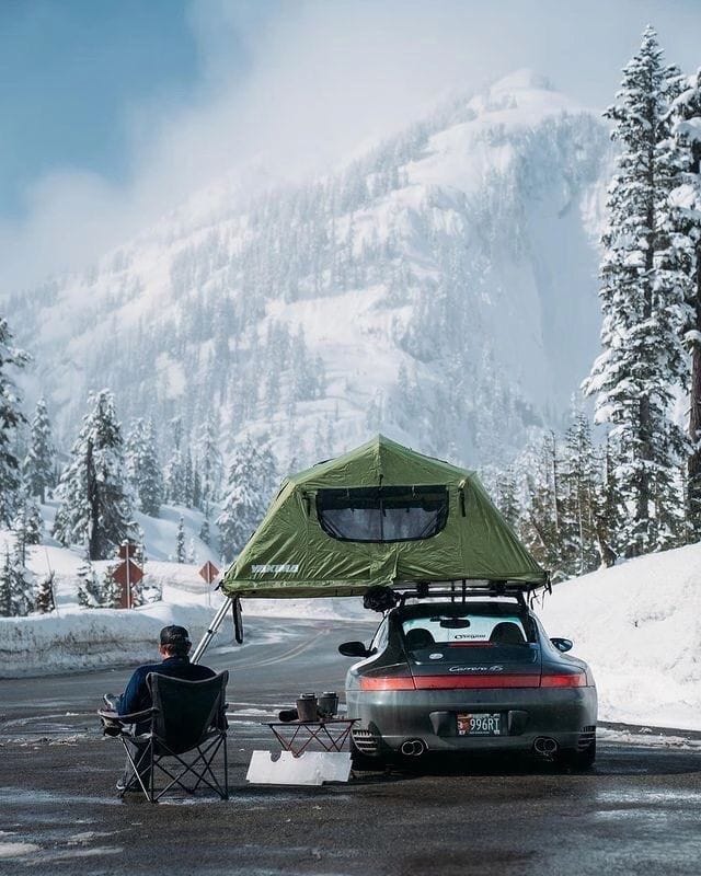 This may contain: a man sitting in a chair next to a car with a tent on top of it This may contain: a man sitting in a chair next to a car with a tent on top of it