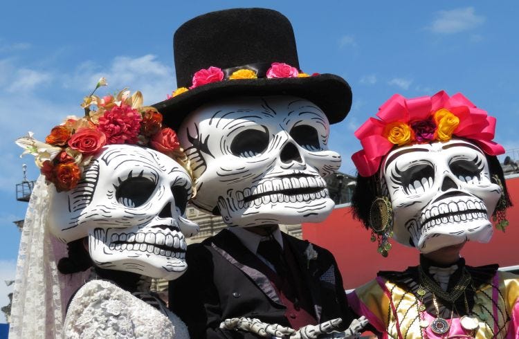Three people dressed as calaveras, or skulls with large skull masks and tradition flowers and clothes celebrating Day of the Dead. Tres personas vestidas como calaveras, o calaveras con grandes máscaras de calaveras y flores y ropas tradicionales que celebran el Día de Muertos. Three people dressed as calaveras, or skulls with large skull masks and tradition flowers and clothes celebrating Day of the Dead. Tres personas vestidas como calaveras, o calaveras con grandes máscaras de calaveras y flores y ropas tradicionales que celebran el Día de Muertos.