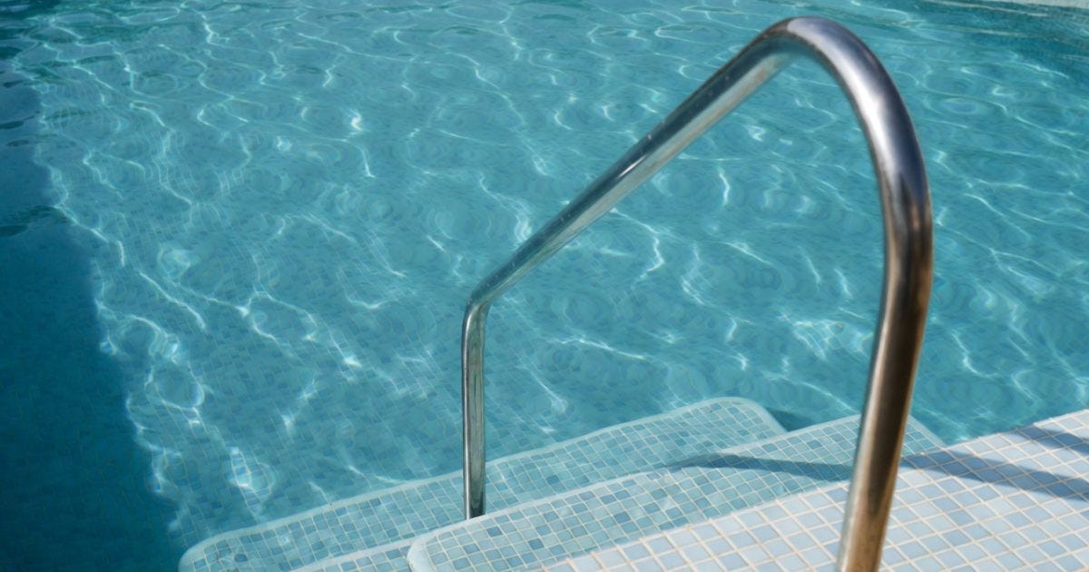 Stainless steel pool ladder leading into clear blue water, highlighting a refreshing swimming pool environment.