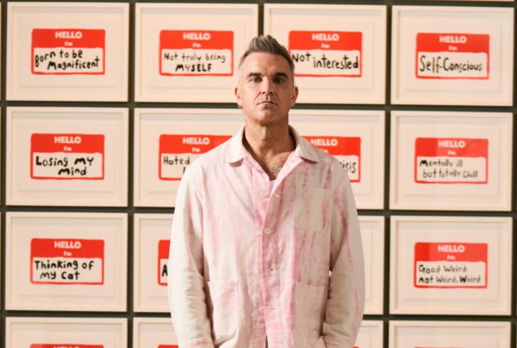 Robbie Williams standing in front of his artworks