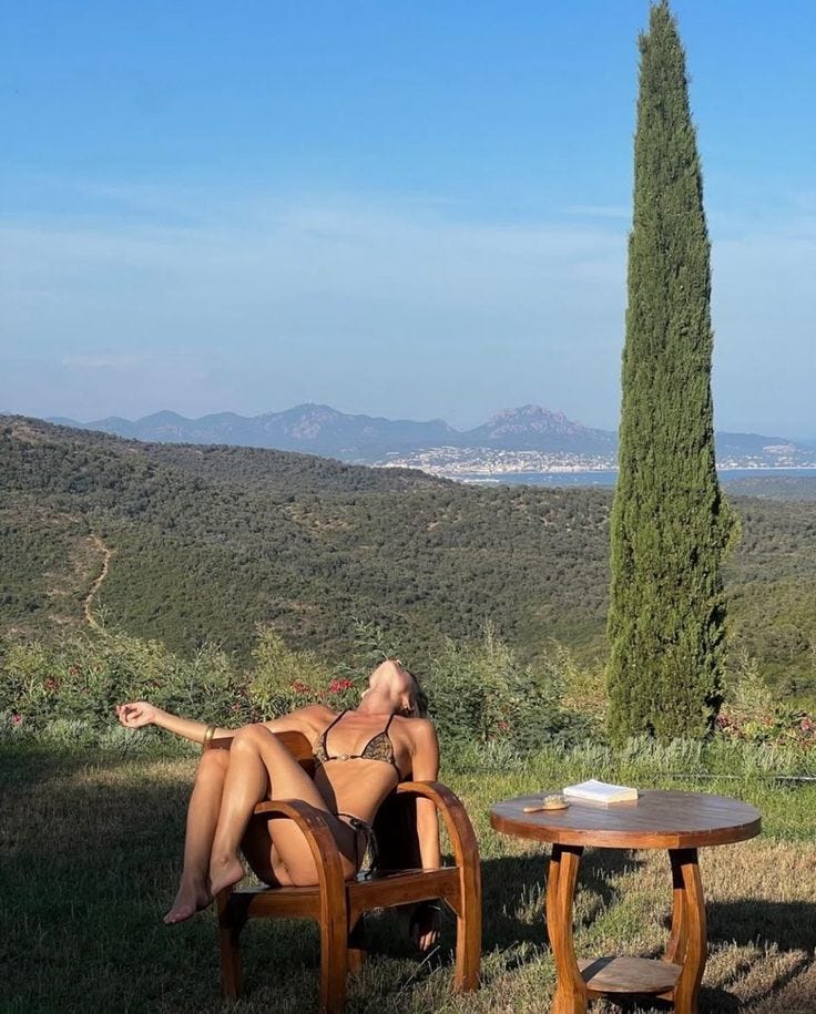 This may contain: a woman laying on top of a wooden chair next to a table in the grass