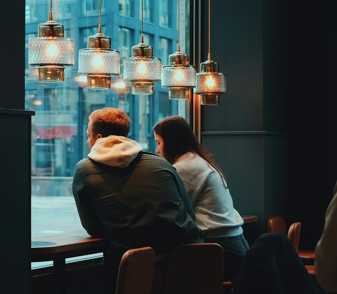 two people sitting at a table looking out a window
