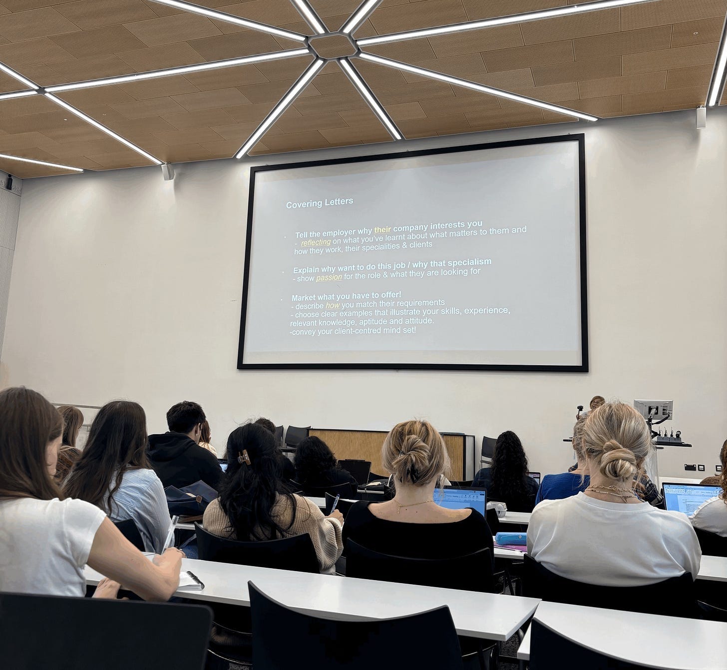 a class with students looking at a projector screen a class with students looking at a projector screen