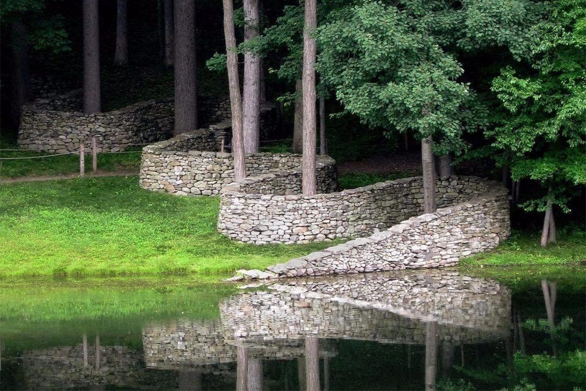 Curving dry-stone wall by Andy Goldsworthy weaving through trees and across a pond at Storm King Art Center in New Windsor, New York.