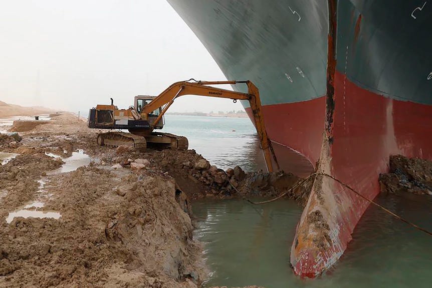 An excavator tries to dig out earth from around the bow of a just stupendously large ship lodged in a bank of the Suez Canal. An excavator tries to dig out earth from around the bow of a just stupendously large ship lodged in a bank of the Suez Canal.
