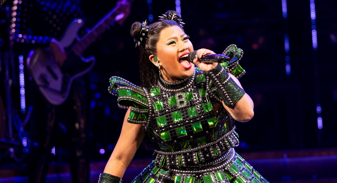 A woman wearing a green bejewelled dress and hair in space buns singing into a microphone