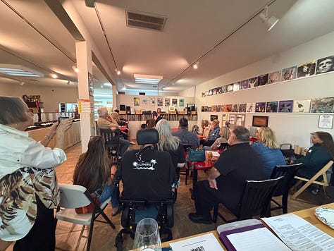 A group of people reading at an open mic inside a small wine bar.
