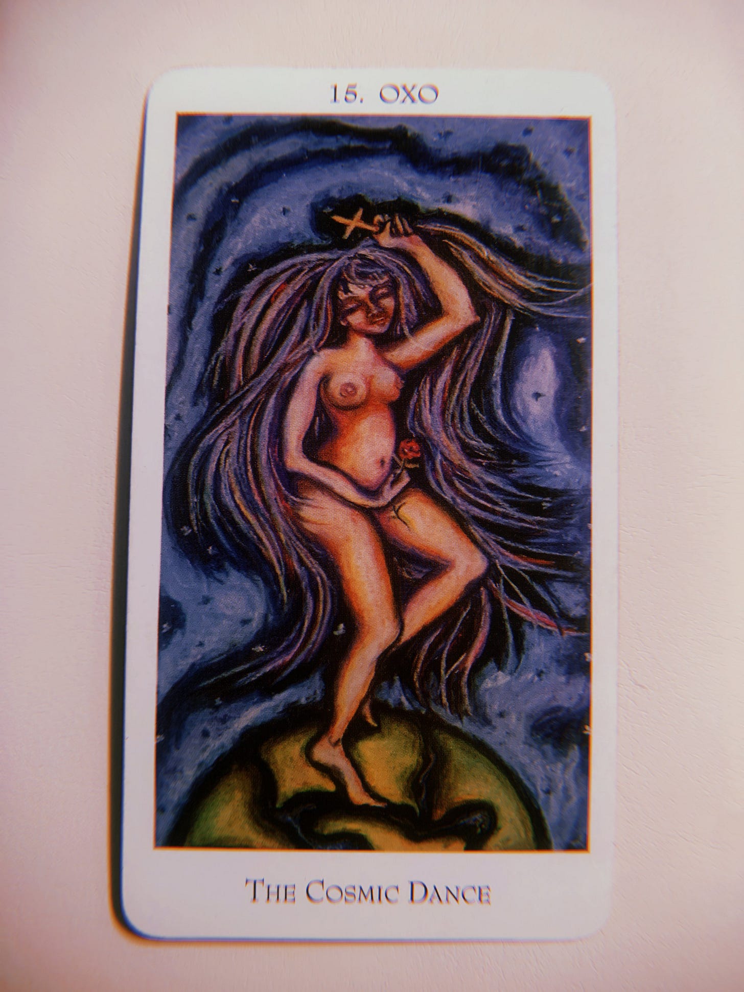 It is a highly saturated image with a cream background. On top is an Enochian Tarot card. A close-up of an Enochian Tarot Card that says 15. OXO The Cosmic Dance. She is depicted as a white woman with abundant purple hair expanding outward. It is a highly saturated image with a cream background. On top is an Enochian Tarot card. A close-up of an Enochian Tarot Card that says 15. OXO The Cosmic Dance. She is depicted as a white woman with abundant purple hair expanding outward.
