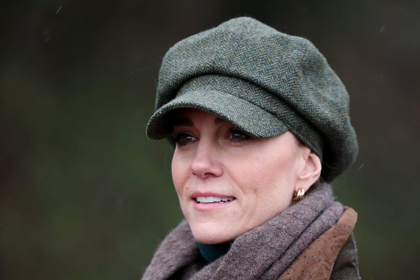 Princess Catherine looking outwards, wearing a green cap and brown scarf
