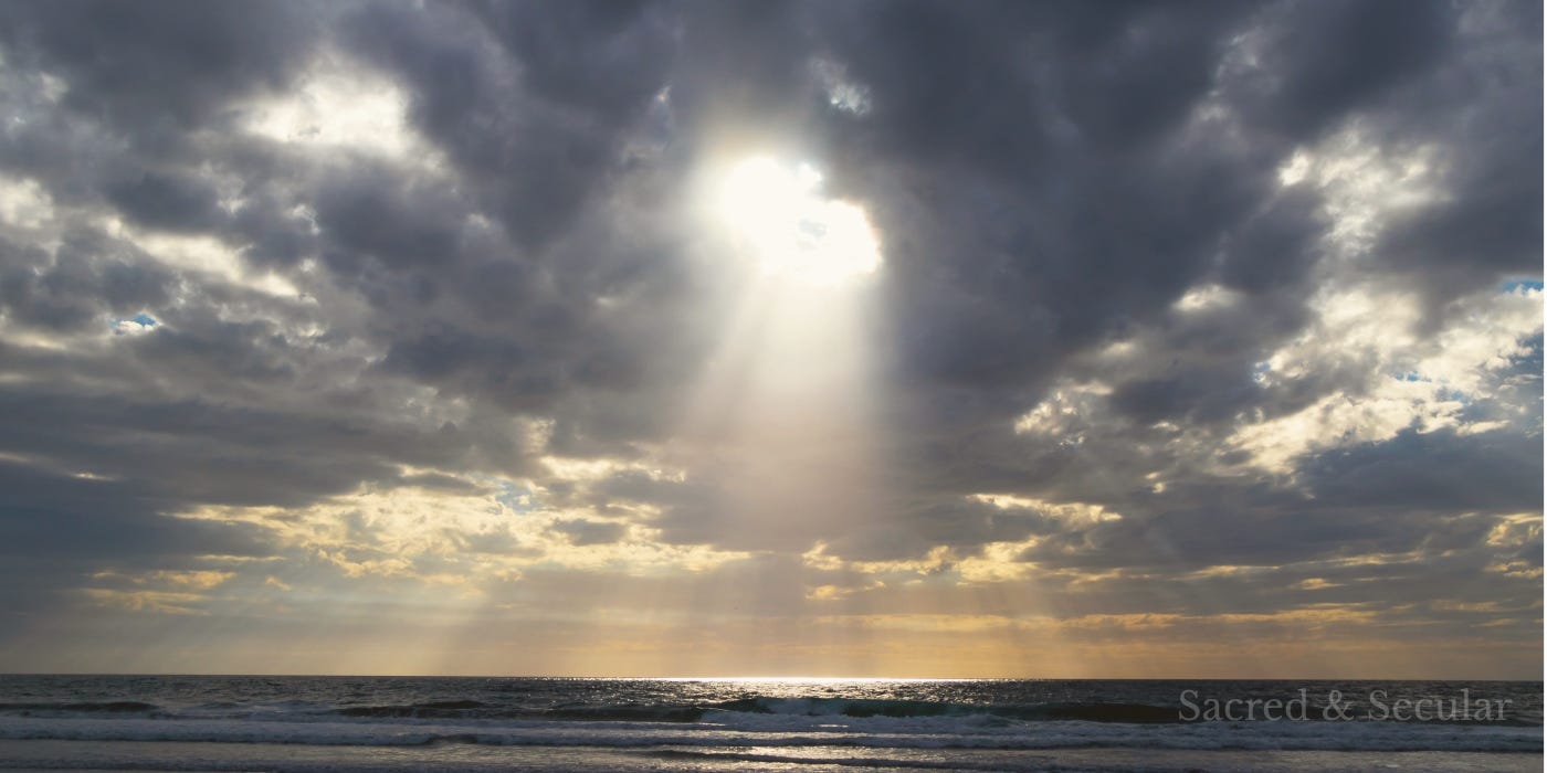 Dark storm clouds over the ocean with bright rays of sunlight breaking through and illuminating the water below.