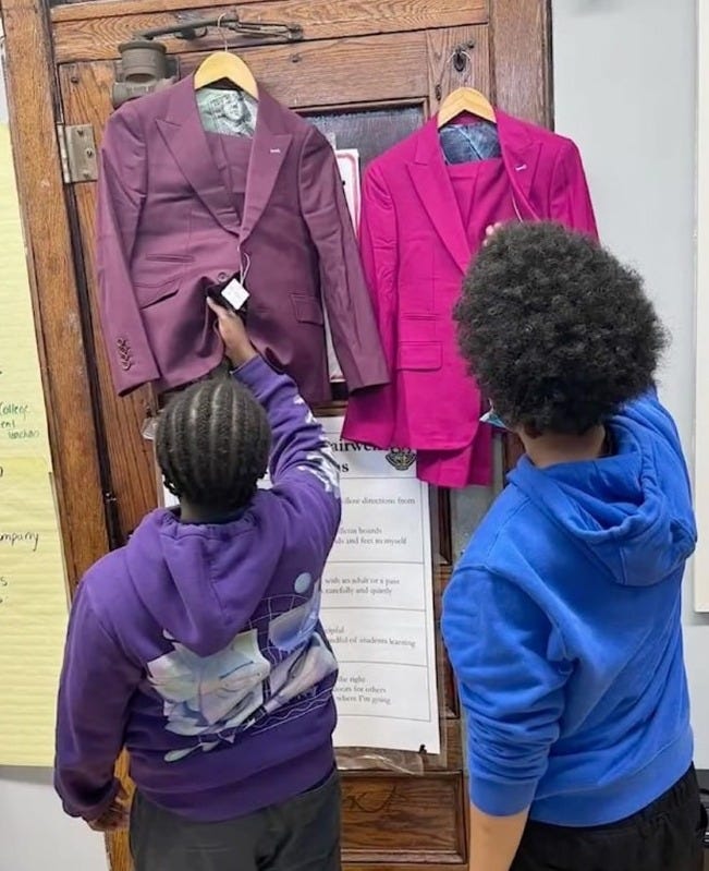 Two young students, their backs to the camera, admire the $650 suits provided in The Modern Day Man program,which come in bright colors like purple and pink