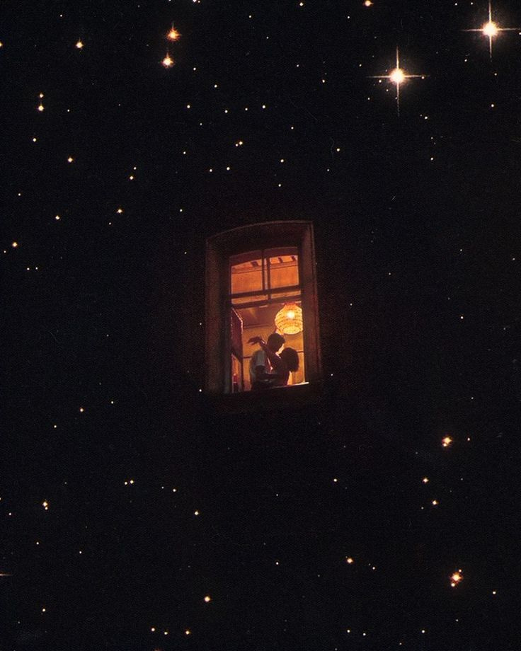 This may contain: two people standing in a window looking out at the stars