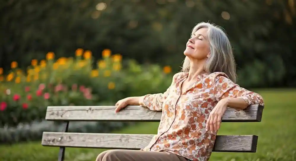 A contented older woman peacefully sits on a park bench soaking up sunshine.