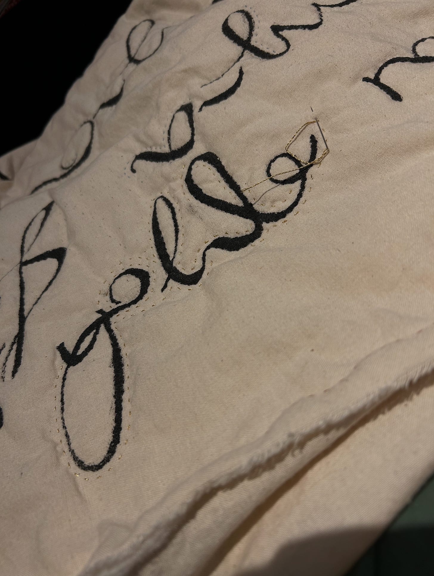 Cream fabric, painted with ink and stitched. A needle holding gold thread is going into the cloth.