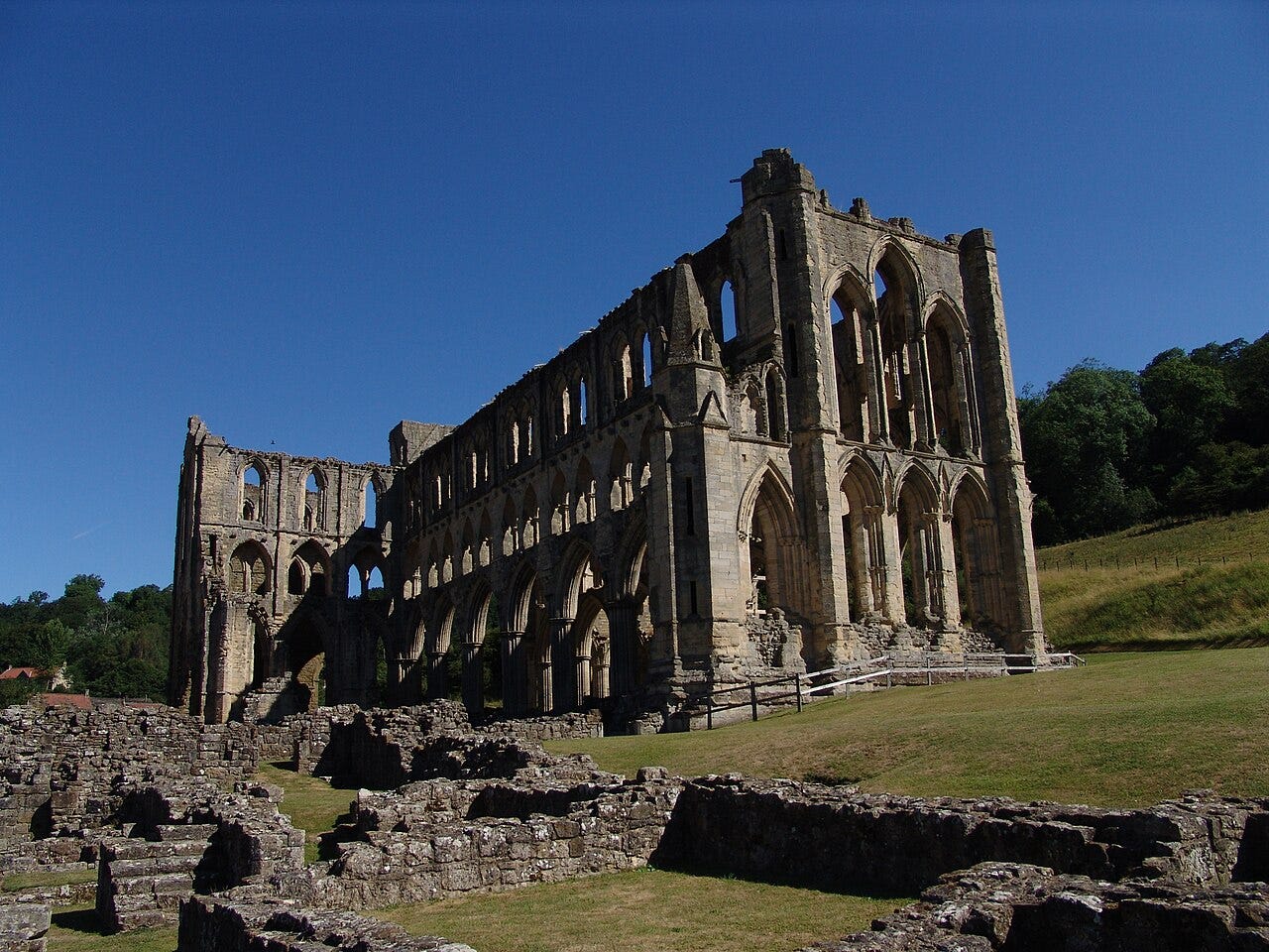 The roofless nave and presbytery of Rievaulx Abbey standing in its wooded valley in Ryedale.