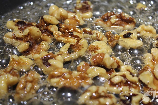 Pecans and walnuts cooking in a sugar and water syrup mixture on the stovetop