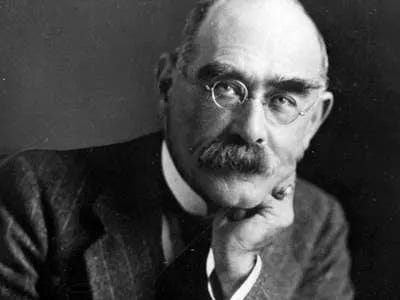 Black and white photograph of Rudyard Kipling, an English poet, balding with a mustache and round wire-rimmed glasses, in a dark suit.