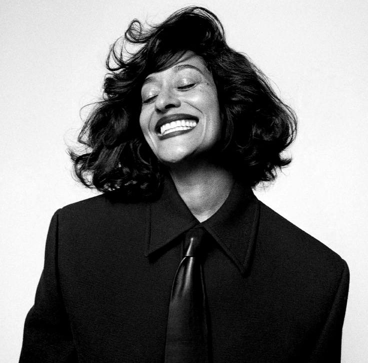 This may contain: a woman wearing a black suit and tie smiling at the camera with her eyes closed