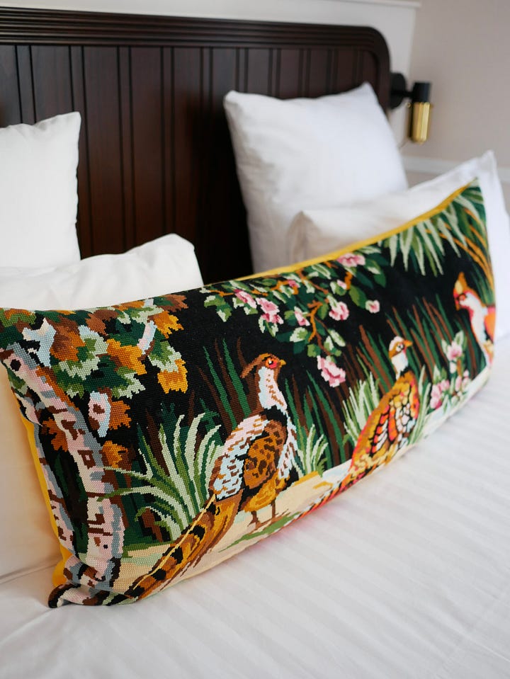 View from Hôtel Chamar in Paris, looking across the streets of St-Georges near Pigalle, with elegant stone buildings and traditional Parisian architecture and decorative embroidered cushion featuring birds and woodland scenes on a bed at Hôtel Chamar in Paris.