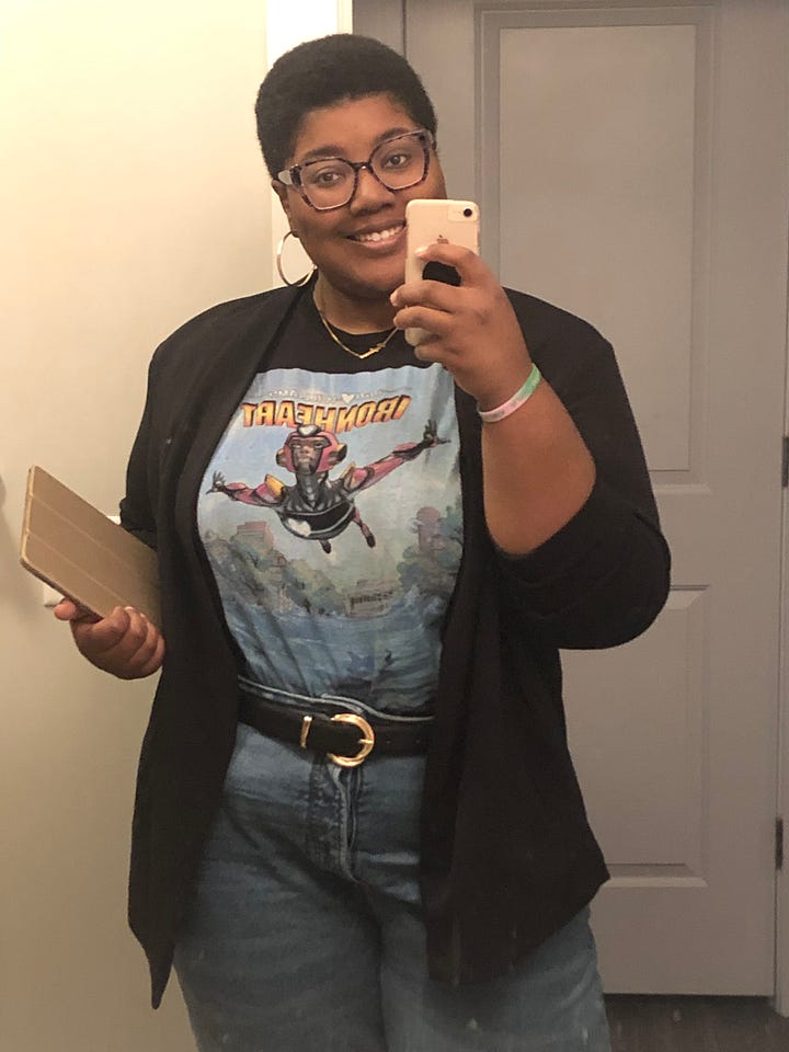 Image 1: Mirror photo of Ravynn in a lilac jumpsuit with a plaid blazer over it and a maroon scarf around her neck; image 2 is Ravynn in a maroon circle skirt and poet sleeve white blouse with a orange plaid cardigan over it and a maroon scarf around her neck and a purple beret on; image 3 is Ravynn in an Ironheart t-shirt, black blazer, and belted jeans; Image 4 is Ravynn in a feminist writers shirt with belted black jeans and a plaid blazer over top.