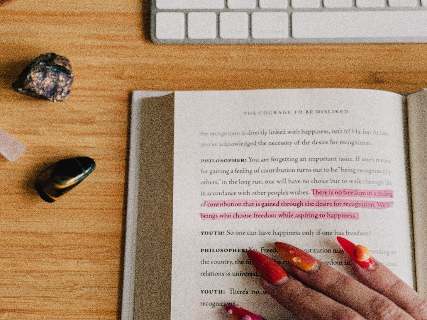 Le livre Avoir le courage de ne pas être aimé ouvert sur un bureau en bois, un passage surligné en rose, une main aux ongles rouges qui pointe la page.