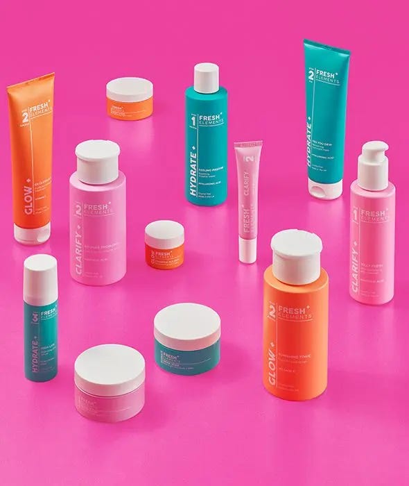 A colorful product shot of the M&S Fresh Elements skincare range for teenagers. The collection features various bottles and tubes in bright pink, teal, and orange packaging, labeled with "Glow," "Hydrate," and "Clarify." The products are arranged on a matching bright pink background, showcasing a modern, age-appropriate aesthetic for Gen Alpha consumers.