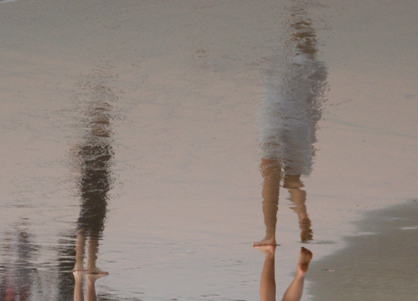 Distorted reflection of two people walking on the beach, symbolizing how children mirror us in ways shaped by what we carry.