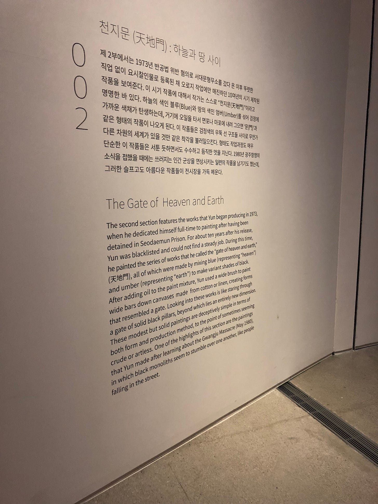 The museum description for The Gate of Heaven and Earth Series. It says, “The second section features the works that Yun began producing in 1973, when he dedicated himself full-time to painting after having been detained in Seodaemun Prison. For about ten years after his release, Yun was blacklisted and could not find a steady job. During this time, he painted the series of works that he called the "gate of heaven and earth," all of which were made by mixing blue (representing "heaven" and umber (representing "earth") to make variant shades of black. After adding oil to the paint mixture, Yun used a wide brush to paint wide bars down canvases made from cotton or linen, creating forms that resembled a gate. Looking into these works is like staring through a gate of solid black pillars, beyond which lies an entirely new dimension. These modest but solid paintings are deceptively simple in terms of both form and production method, to the point of sometimes seeming crude or artless. One of the highlights of this section are the paintings that Yun made after learning about the Gwangju Massacre (May 1980), in which black monoliths seem to stumble over one another, like people falling in the street.