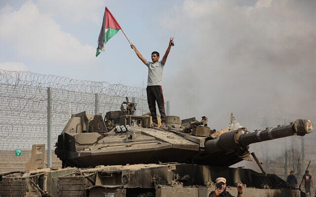 A Palestinian stands on an Israeli tank at the border fence near the city of Khan Younis in the southern Gaza Strip after some 3,000 Hamas terrorists burst through the border and entered Israel, slaughtering some 1,200 people, October 7, 2023. (Yousef Mohammed/Flash90) A Palestinian stands on an Israeli tank at the border fence near the city of Khan Younis in the southern Gaza Strip after some 3,000 Hamas terrorists burst through the border and entered Israel, slaughtering some 1,200 people, October 7, 2023. (Yousef Mohammed/Flash90)