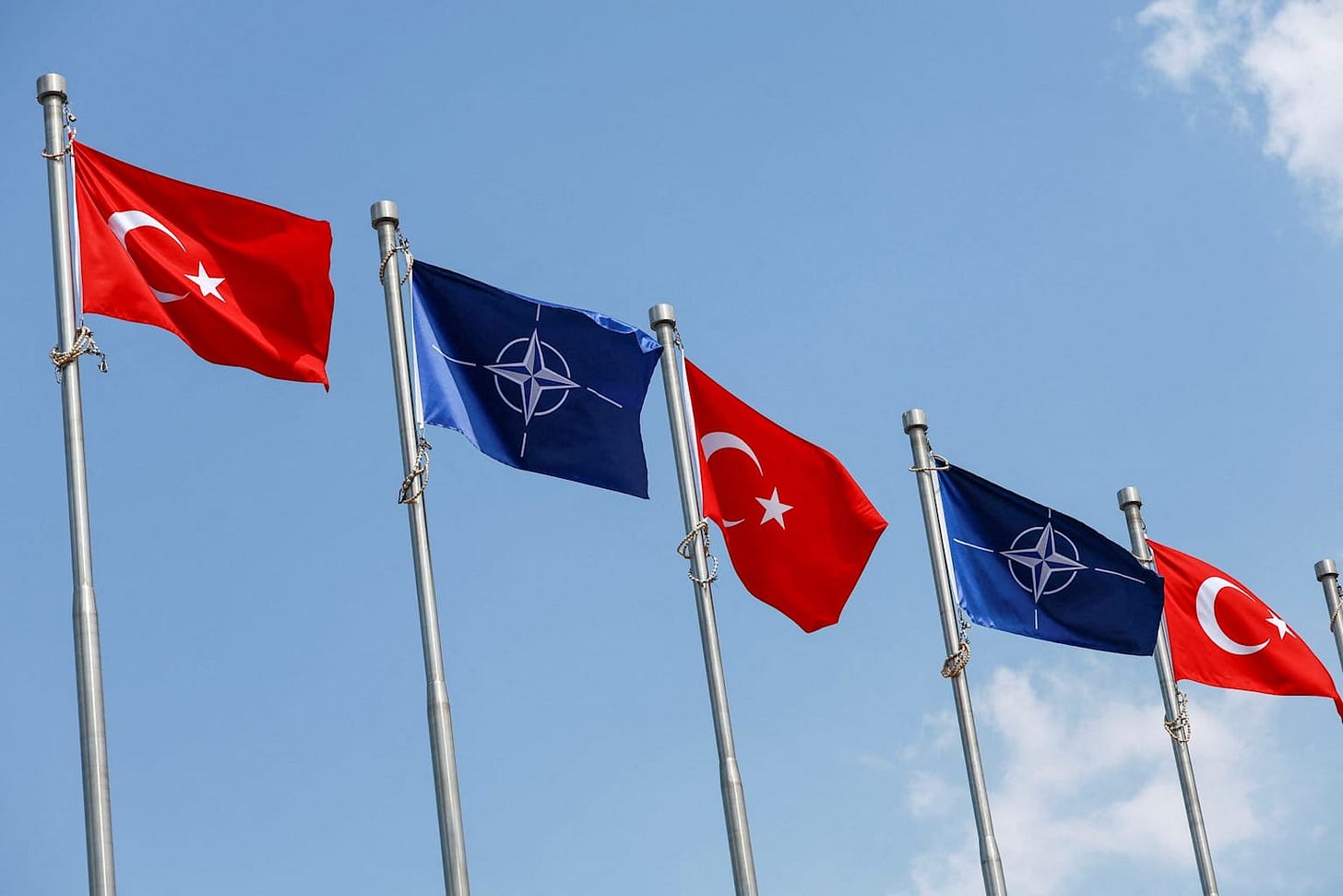 Turkish and NATO flags flying against a blue sky ahead of the Ankara summit