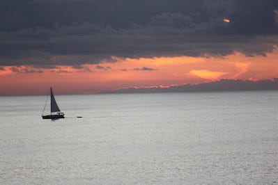 Sunset over the water with  sailboat nearby