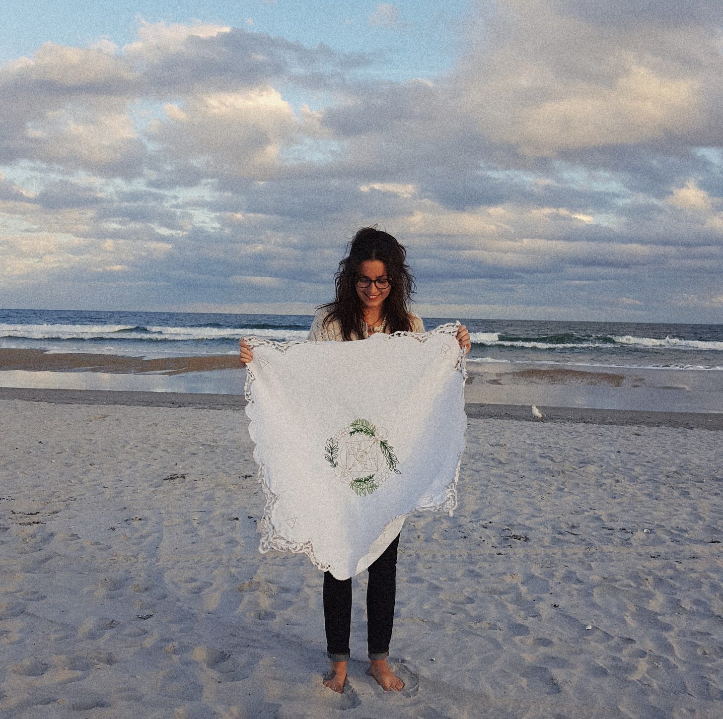 brunette woman on a beach smiling and holding a tapestry in front of the clouds and crashing waves brunette woman on a beach smiling and holding a tapestry in front of the clouds and crashing waves
