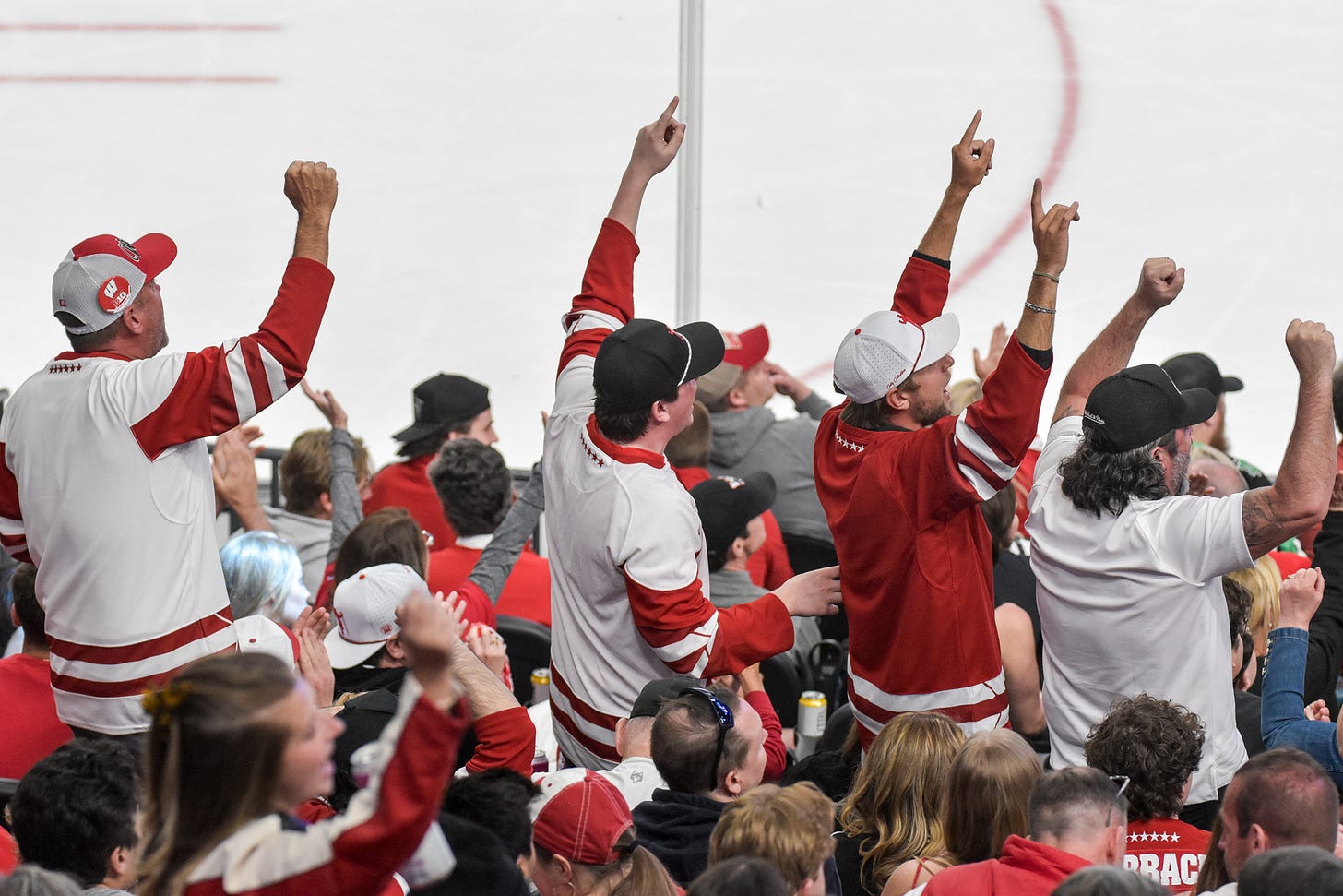 Four Wisconsin Badger fans holler as their team leads 1-0 over Denver in the national championship game. Fists raised in air.