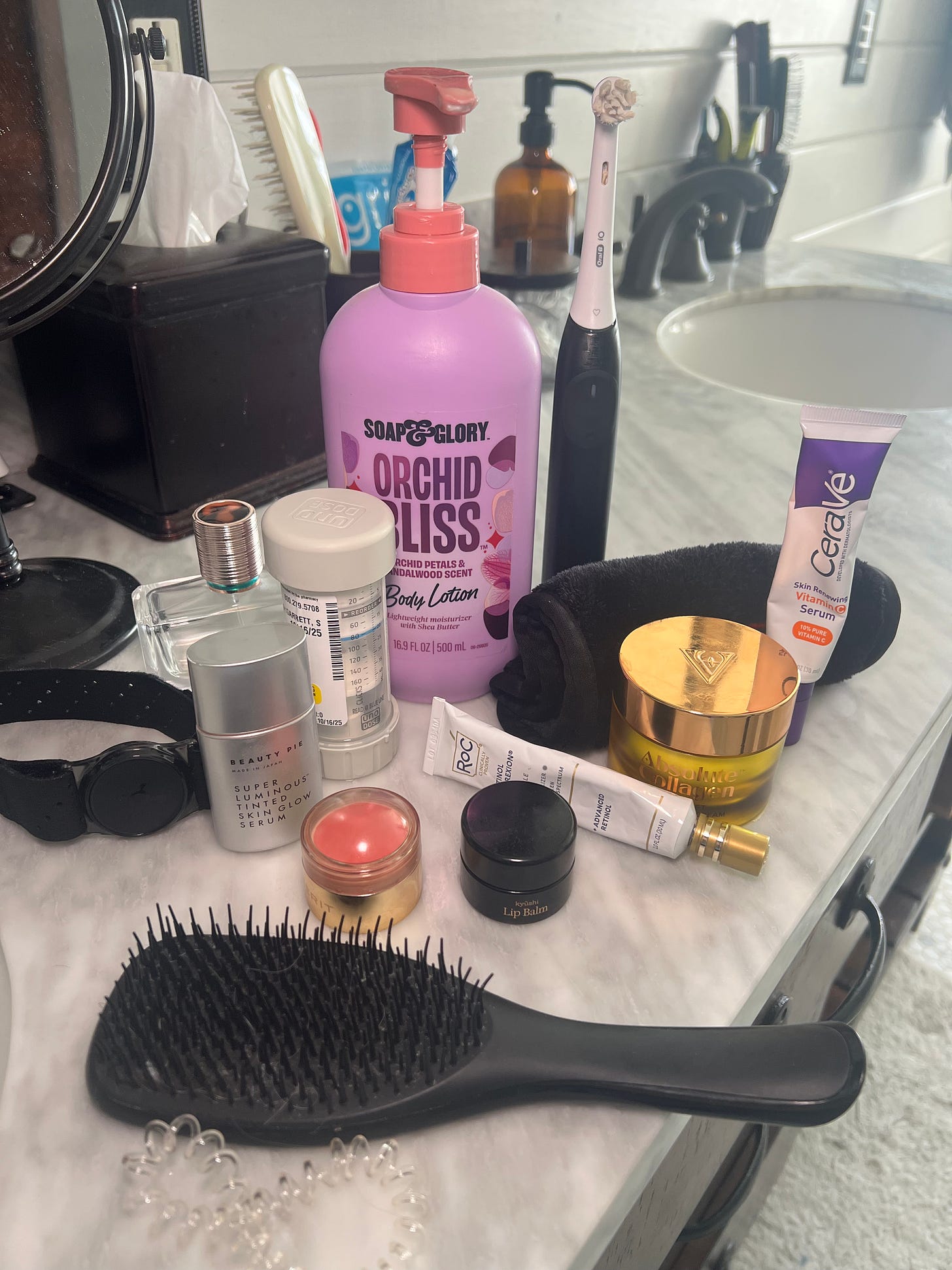 The Beauty Ed® "Carry-On" edit: A flatlay of beauty products on a white marble surface, featuring Donna Francis’s current favorites like RoC Retinol Correxion, Kyushi Lip Balm, and a bottle of fragrance, neatly arranged next to everyday essentials.