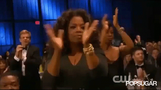 Audience at award show stsnding and clapping, with Oprah standing in the front row