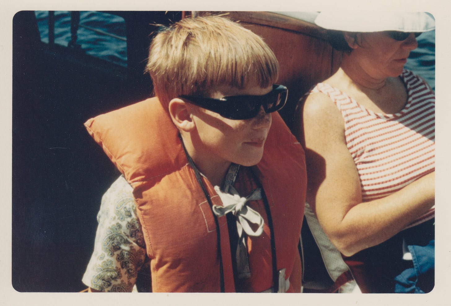 Boy in sunglasses and orange life preserver with his mother in an orange-striped top.