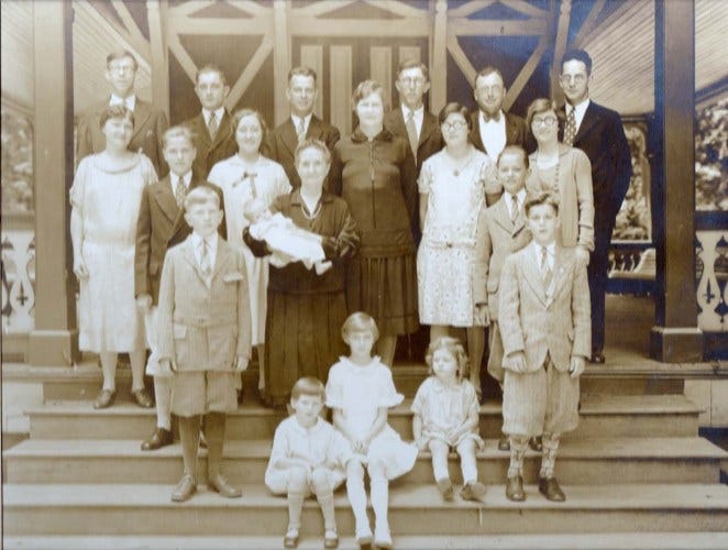 Vintage sepia-toned family group portrait on church steps, adults and children in 1930s-1940s formal attire.