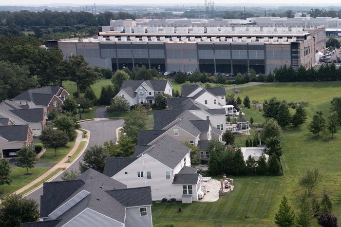 Aerial view of a large Amazon Web Services (AWS) data center building next to single-family homes.
