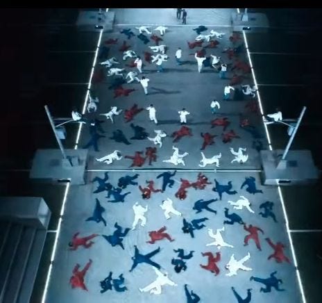 Stage of Kendrick Lamar’s half time show, performers dressed in red white and blue pose as corpses.