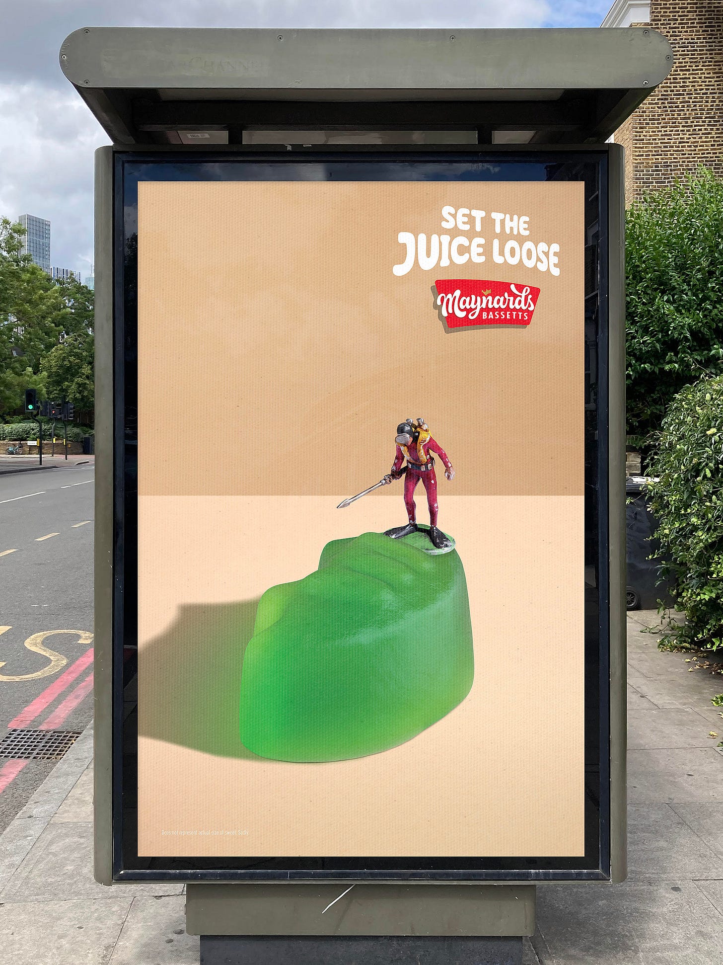 Poster showcasing a miniature model diver with a harpoon standing on top of a green winegum in the centre of the poster. Logo for Maynards Bassetts with endline saying set the juice loose in top right corner. 
The concept is to leave the viewer to imagine that when the harpoon pierces the skin of the sweet it would set the juice loose much like the explosion of flavour that happens in your mouth when eating Winegums.