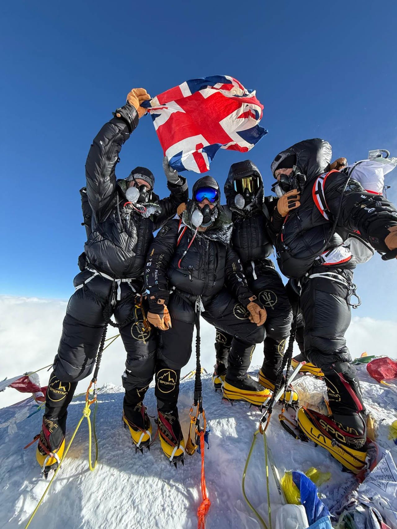 Four British climbers on a mountain summit holding a Union Jack flag.