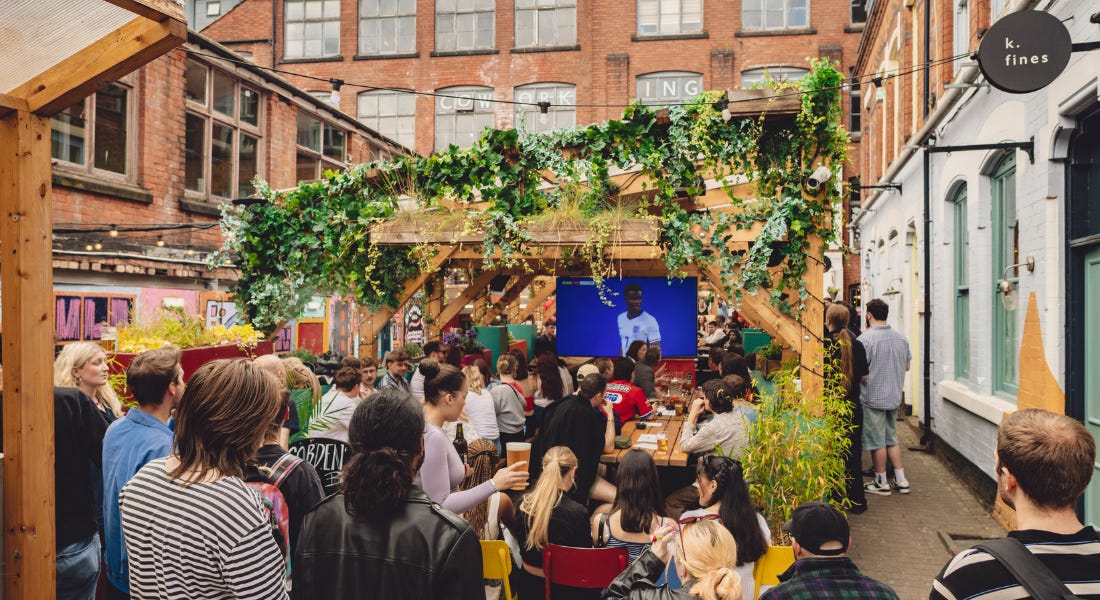 A group of people standing outside watching a tv screen with wooden beams above them A group of people standing outside watching a tv screen with wooden beams above them