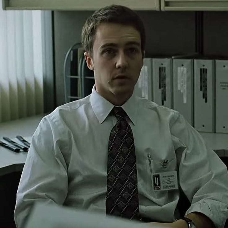 This may contain: a man sitting at a desk in an office wearing a white shirt and black tie