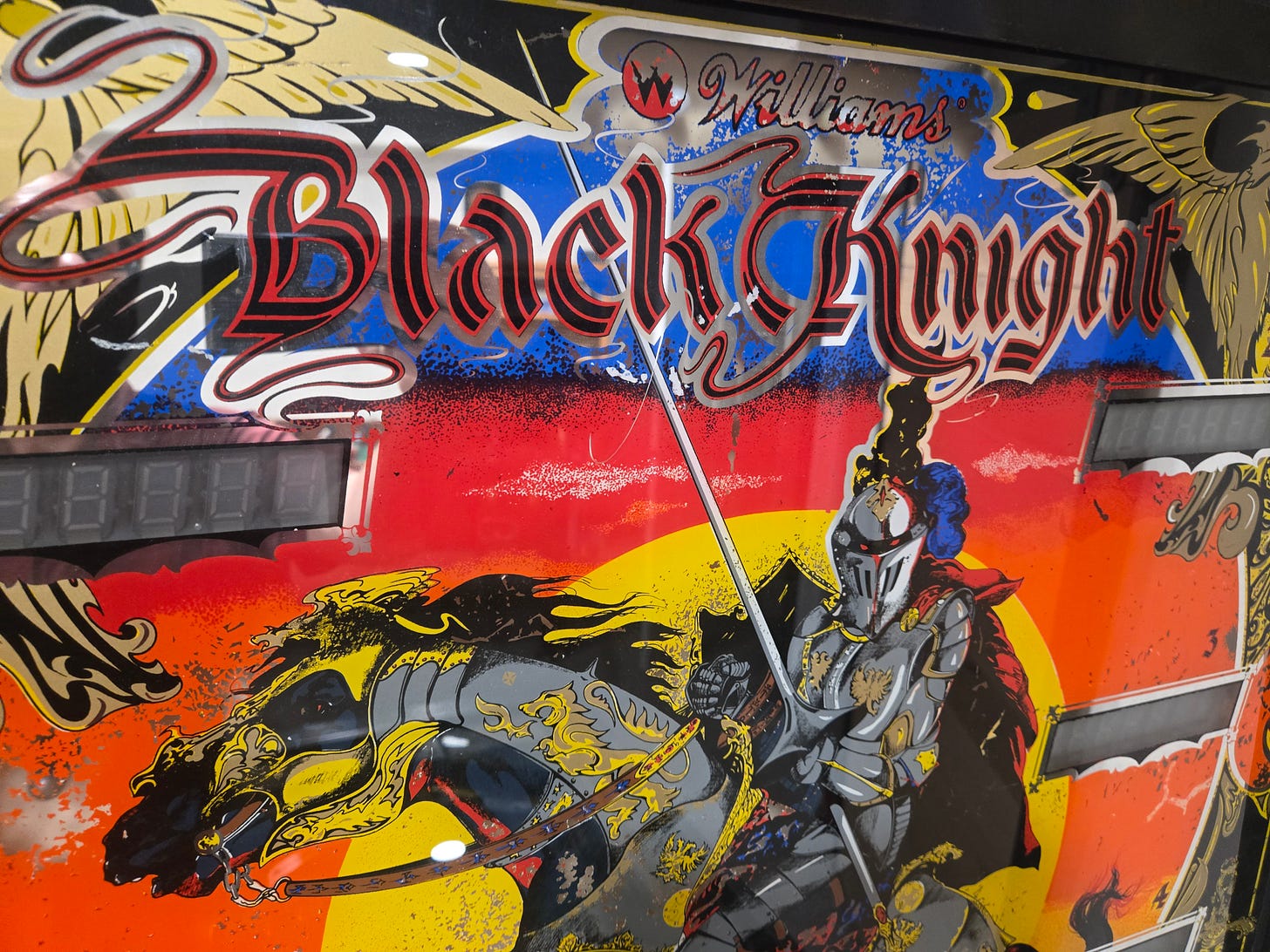 Close-up of the Williams Black Knight (1980) backglass art showing the 'Black Knight' title lettering, knight on horseback with lance, and scoreboard display Close-up of the Williams Black Knight (1980) backglass art showing the 'Black Knight' title lettering, knight on horseback with lance, and scoreboard display