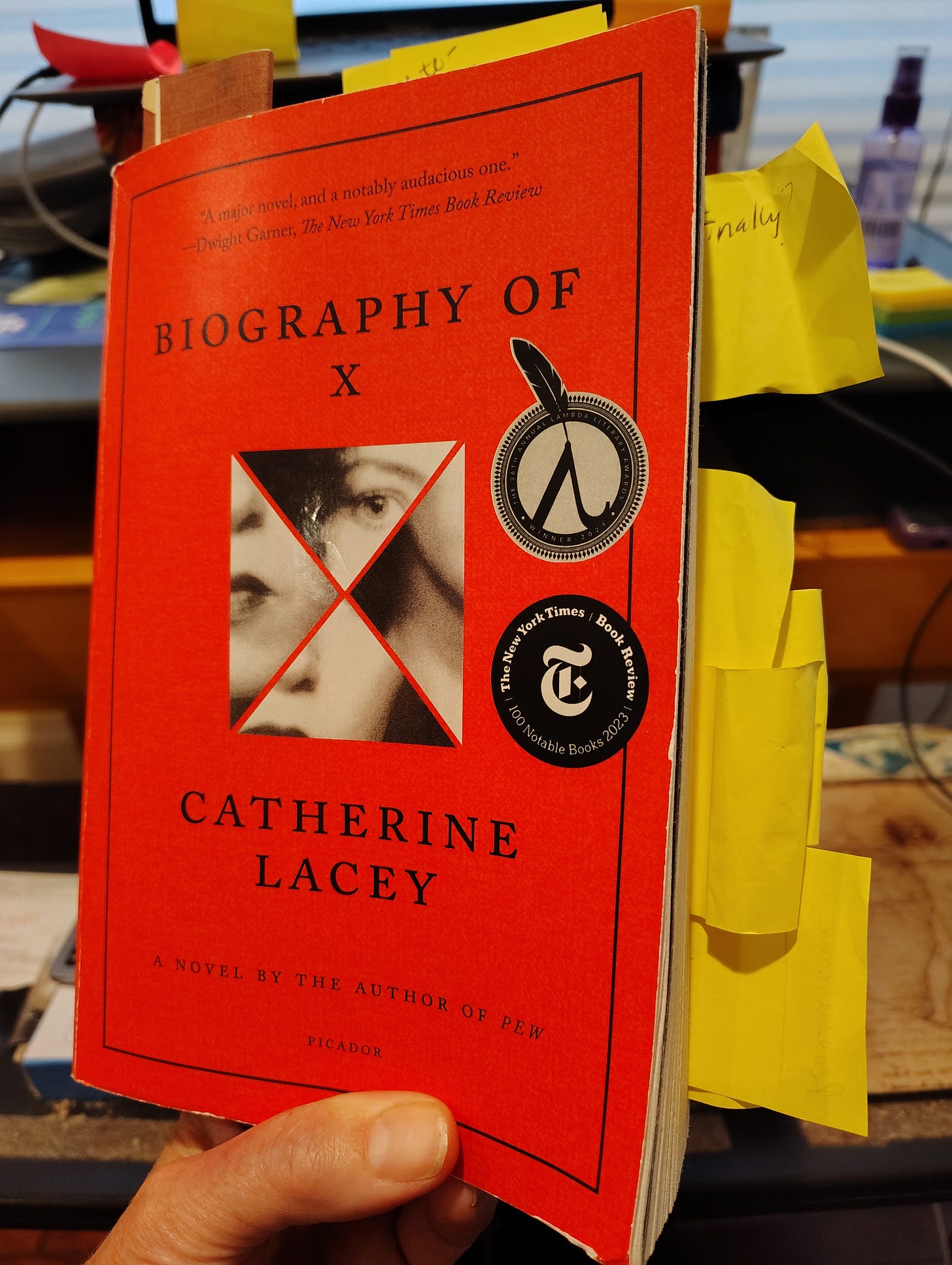 Biography of X a red paperback book held in a hand with sticky notes and bookmark protruding from the top and side edges