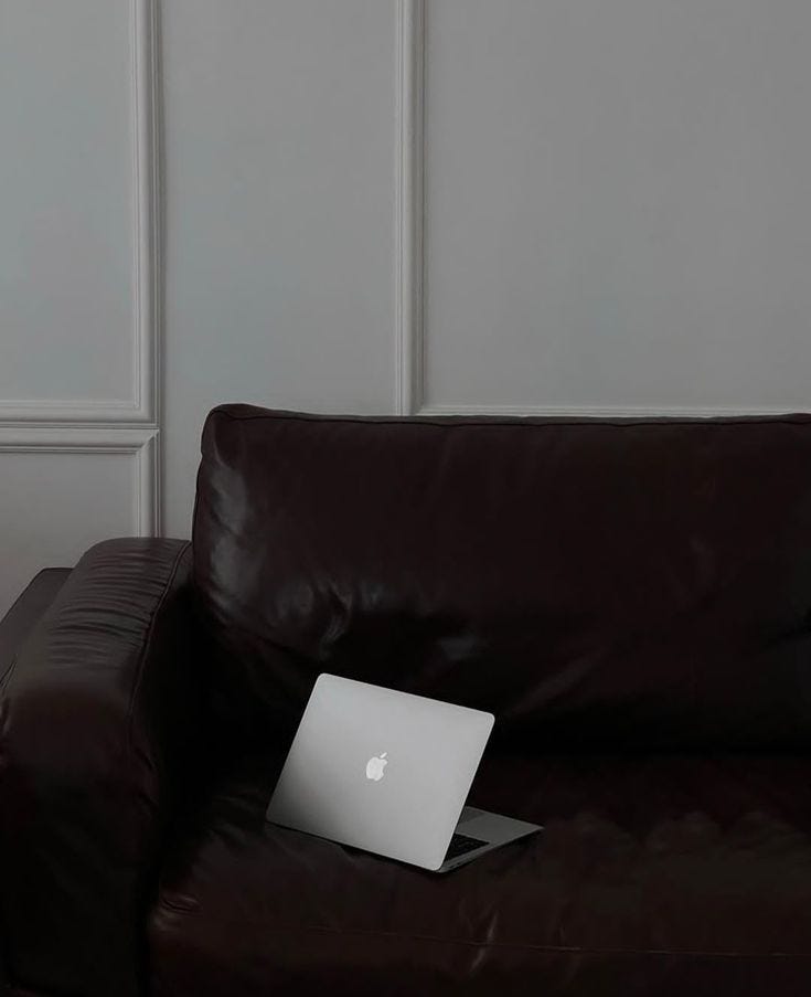 This may contain: an apple laptop sitting on top of a brown leather couch in front of a white wall