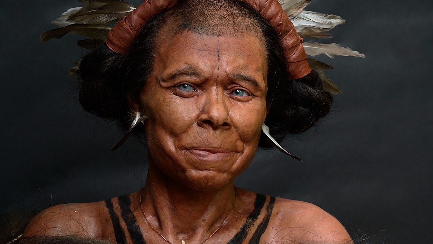 A reconstruction of a Stone Age woman with tattoos along her collarbones and nose and a headdress and jewelry made of feathers, leather and bone 