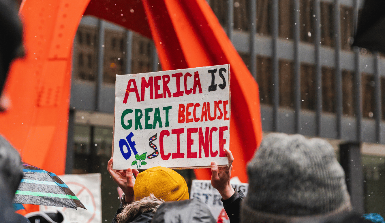  Protest sign reading "America is great because of science" held up in a crowd during a snowy protest.