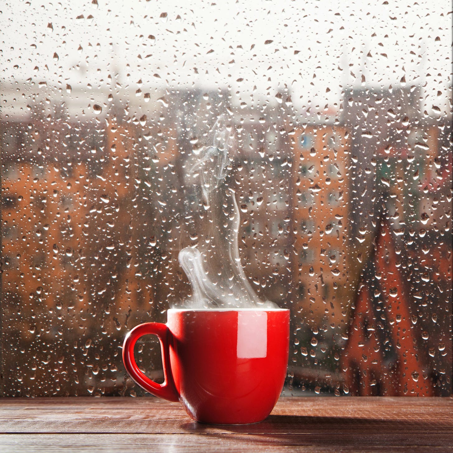 A red coffee cup up against a window covered in rain drops during a storm.